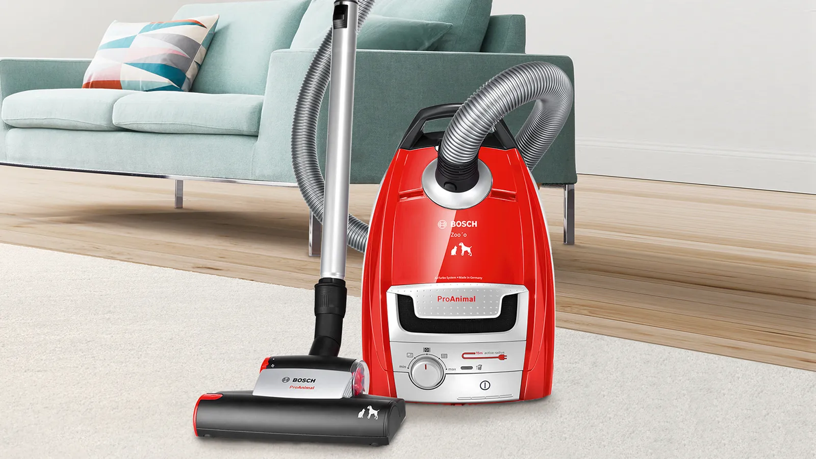 Staubsauger in Rot mit Schlauch und Bedienelementen, auf Holzboden neben einem grünen Sofa platziert.