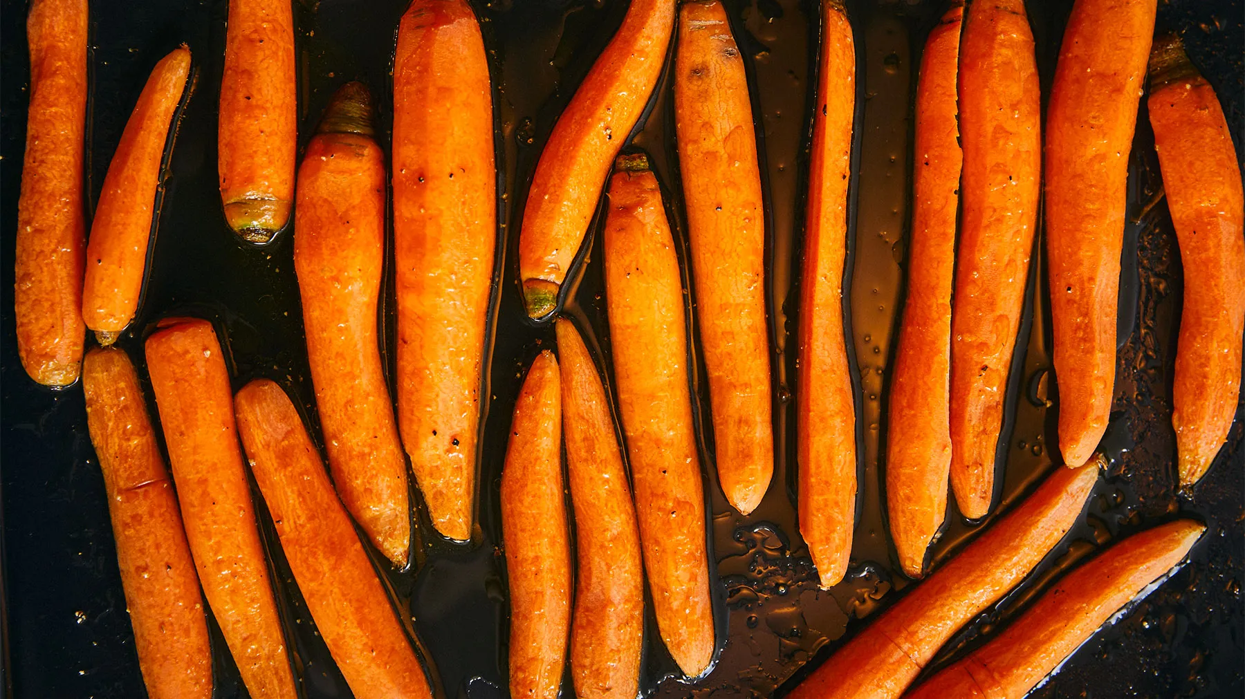 Carote arancio arrosto su una teglia scura, vista ravvicinata.