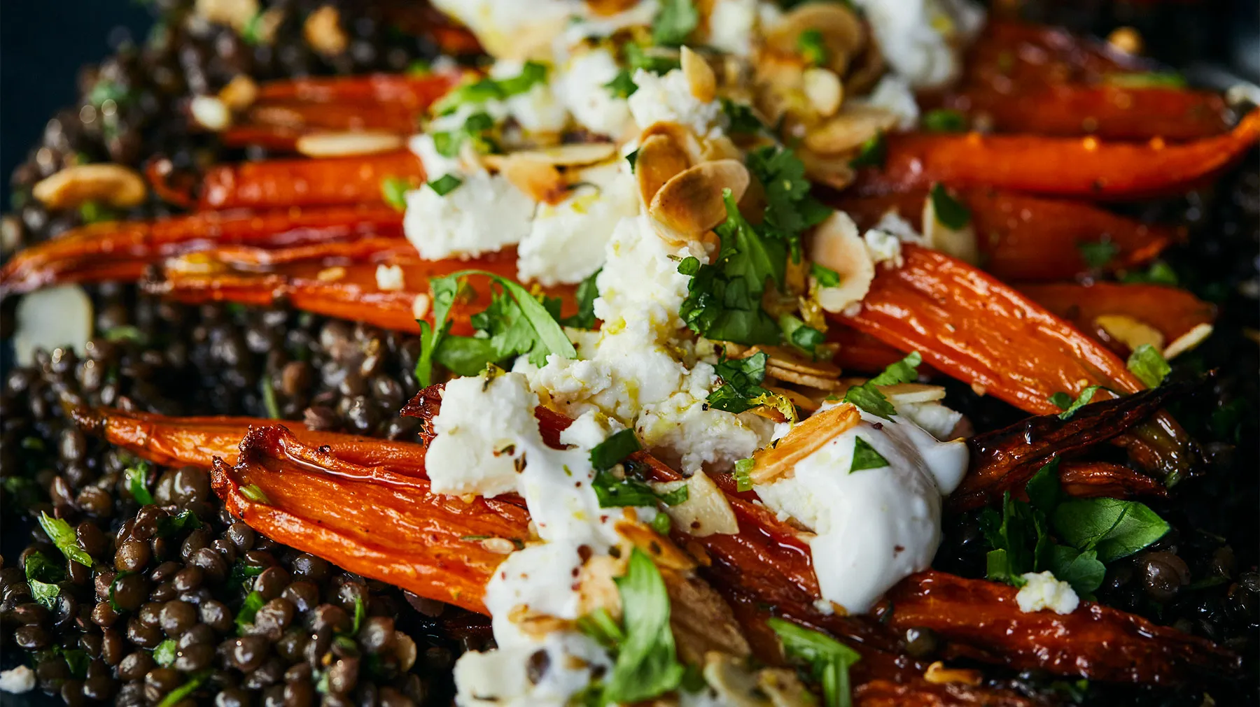 Carote arrosto, lenticchie, feta ed erbe su fondo scuro.