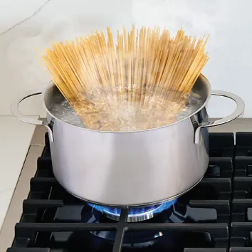 Metal pot on Bosch gas stove with spaghetti boiling over high heat.