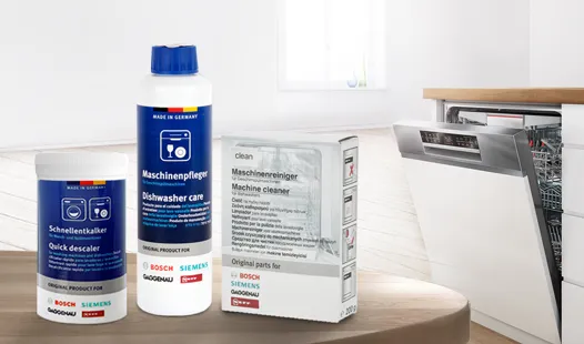 Dishwasher cleaning products, including detergent and cleaner, on a wooden table in a kitchen.