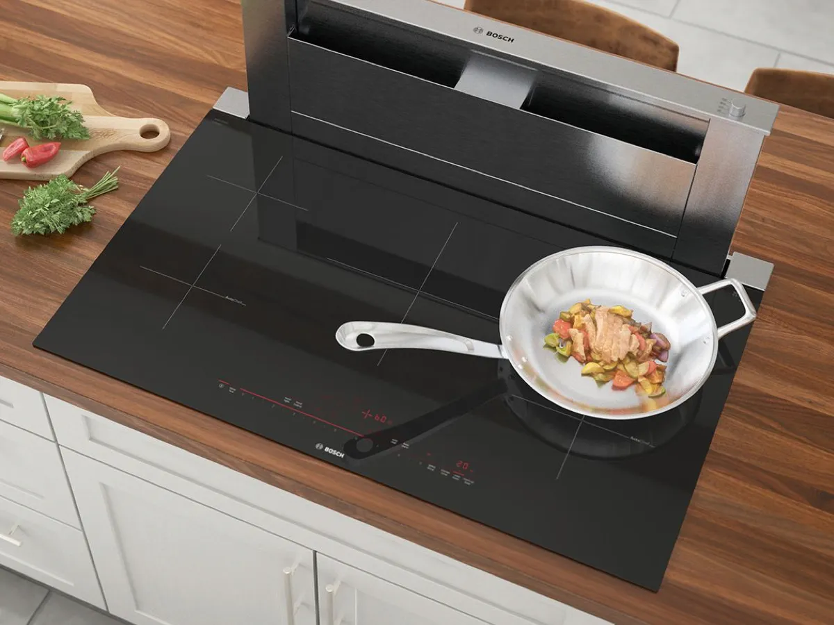 Kitchen countertop with Bosch induction cooktop, stainless steel cooking pan, and fresh ingredients.