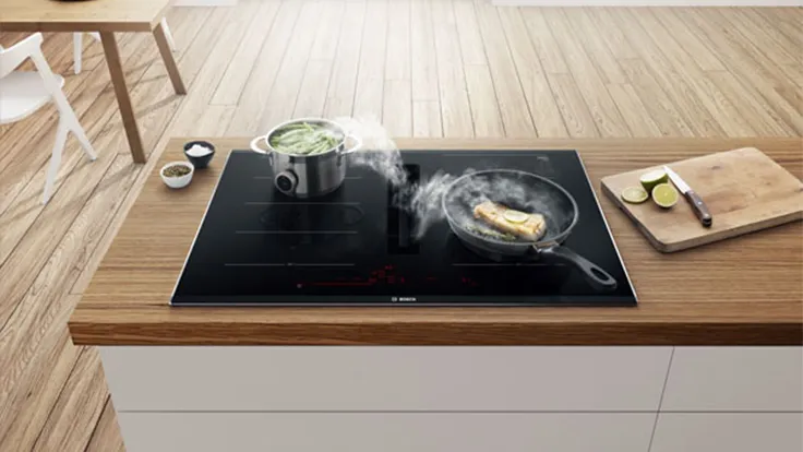 Induktionskoktop med ångande pott och sizzling mat, träköksräknare, minimalistisk inredning.