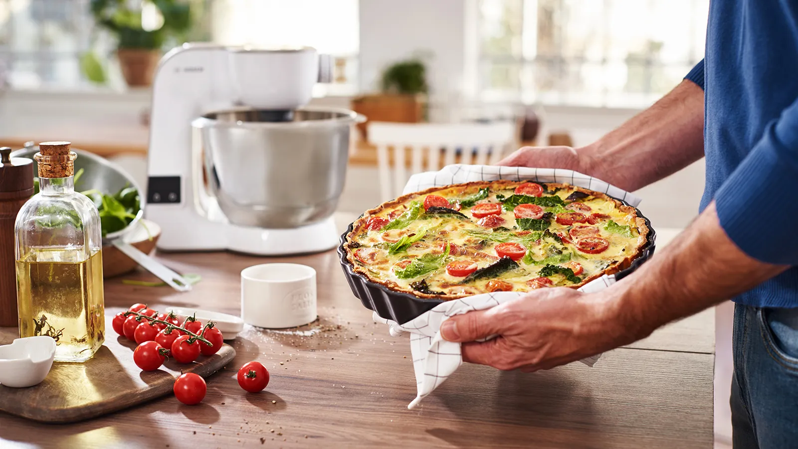 Quiche de casă cu legume, aparate de bucătărie, și ingrediente de gătit pe masă de lemn.