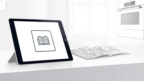 Tablet displaying book icon, papers, and kitchen appliances in background.