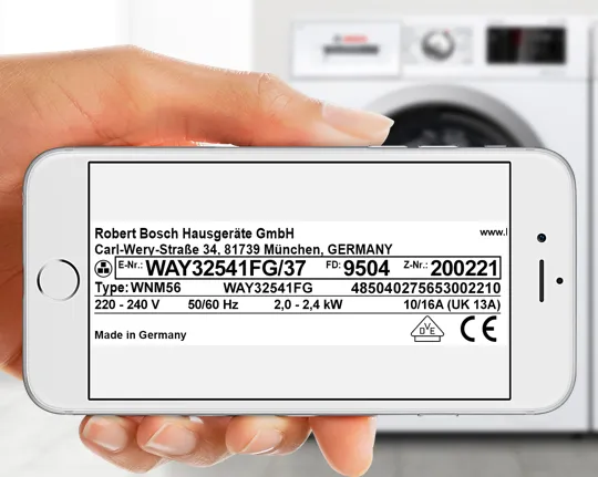 Hand holding smartphone displaying washing machine product information label.