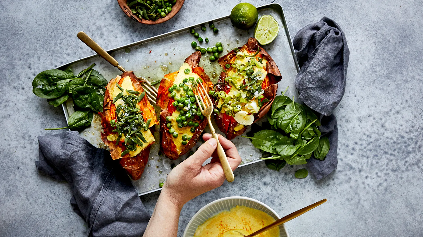 Gegrilltes Gemüsegericht mit Spinat, Limette und Tauchsauce auf grauem Hintergrund.