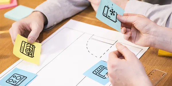 Hands working on paper with icons, sketching, designing, planning, brainstorming, creative process.