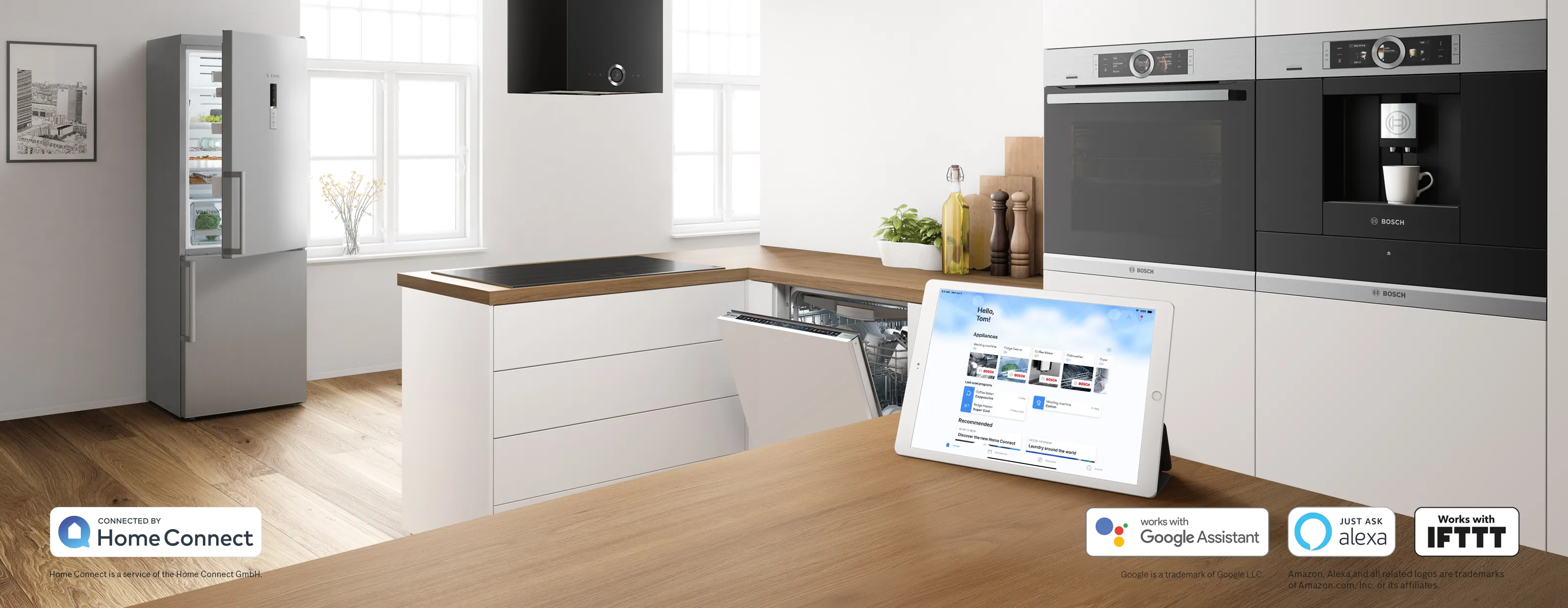 Modern kitchen with smart Bosch appliances, open fridge and dishwasher, and tablet displaying Home Connect app on wooden countertop.