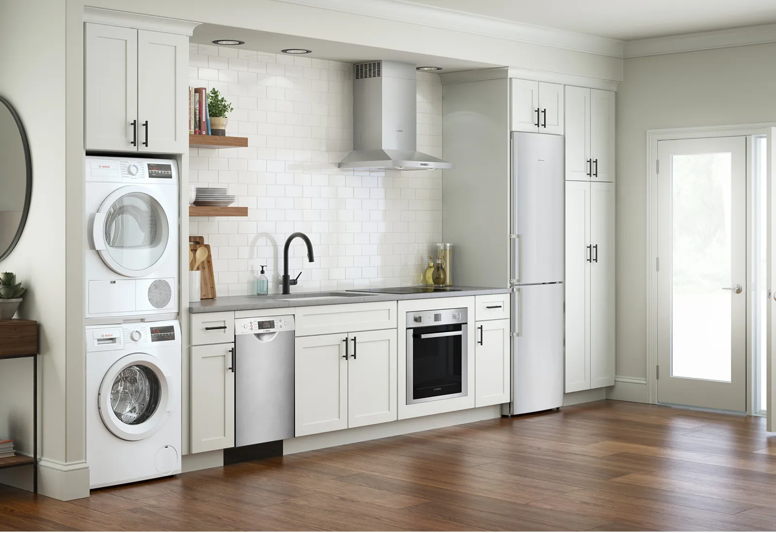 Modern kitchen with white cabinets, Bosch stacked washer and dryer, Bosch stainless appliances, and wood floor.