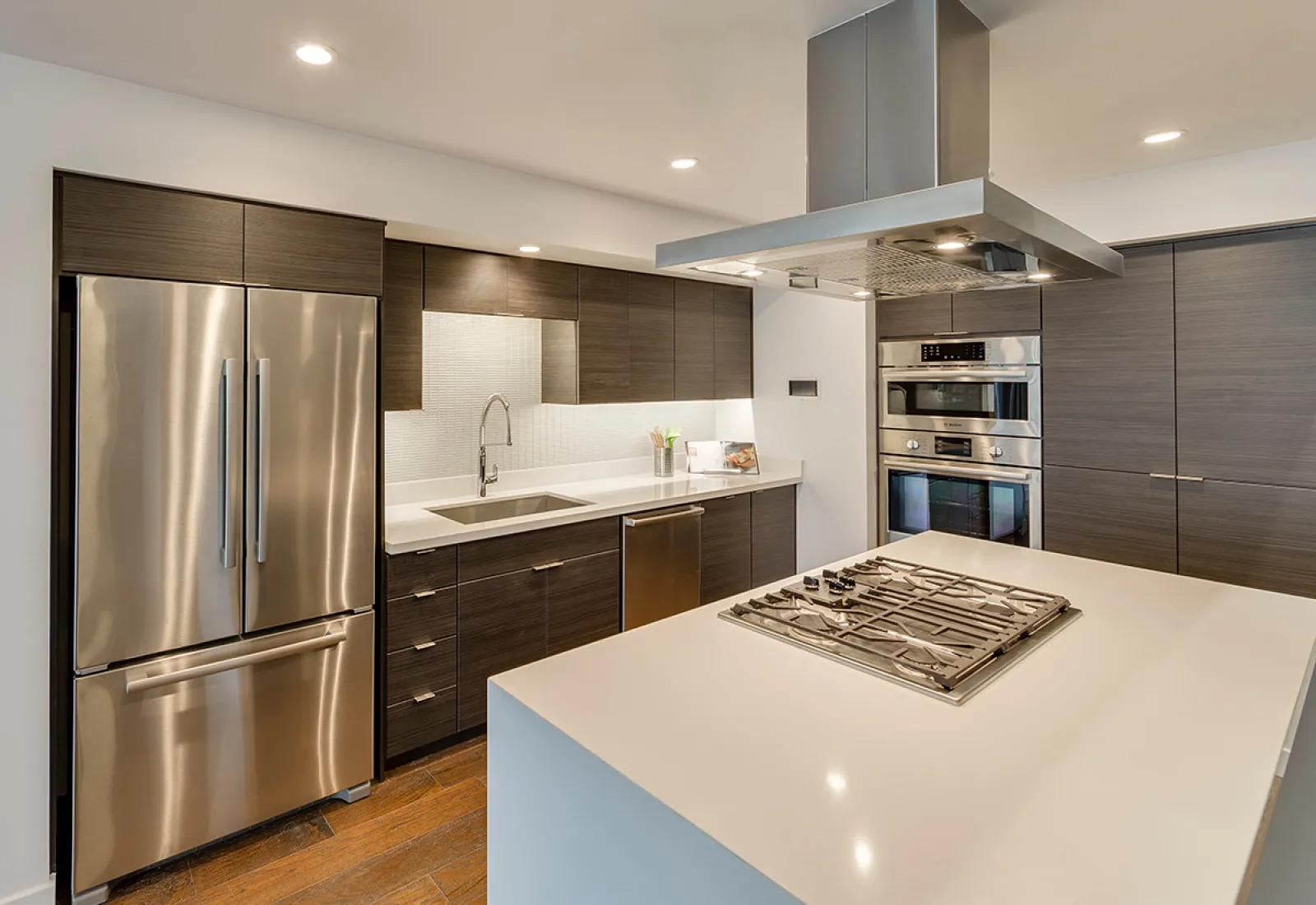 Modern kitchen with stainless steel appliances, dark cabinets, and a white island countertop.