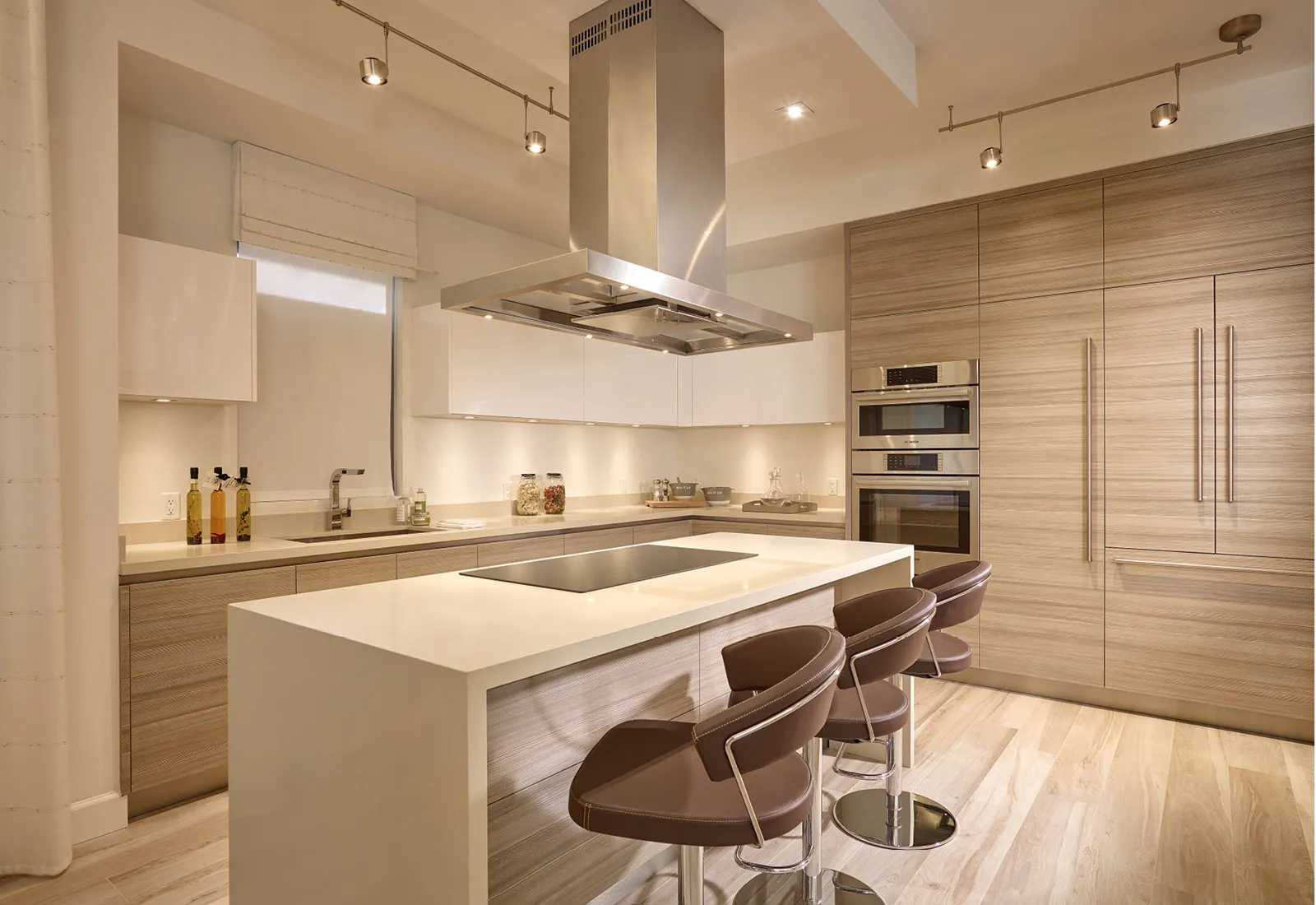 Modern kitchen with a central island, bar stools, and Bosch built-in appliances in light wood decor.