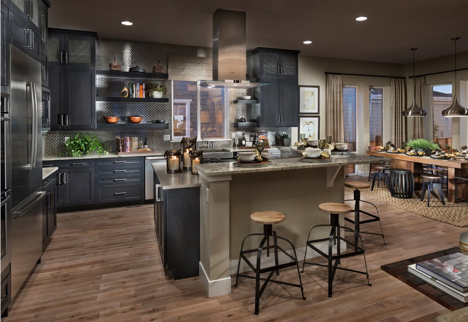 Modern kitchen with dark cabinets, island, bar stools, and open dining area with pendant lights.