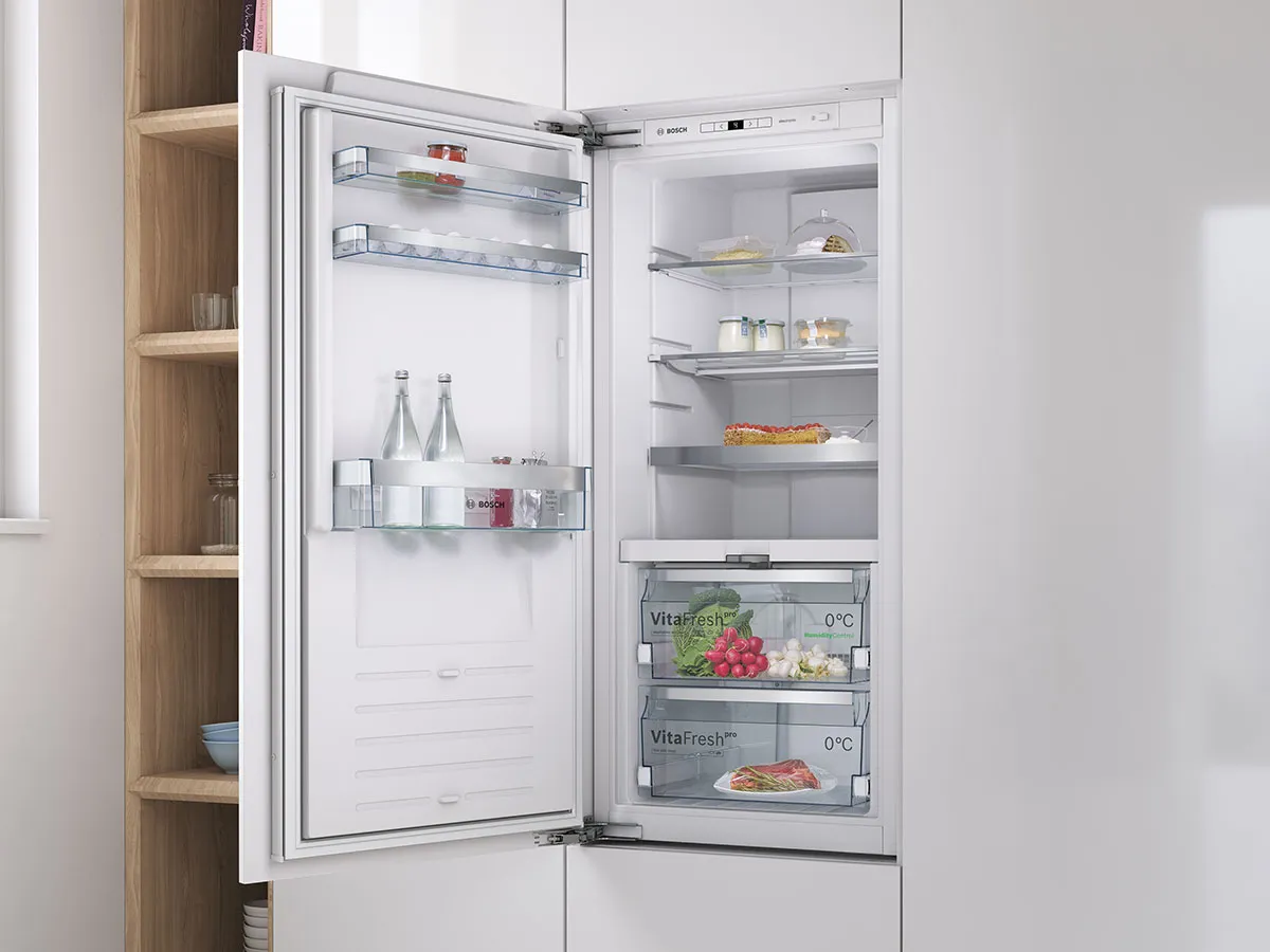 Frigorifero da incasso con porta aperta che mostra ripiani con bottiglie, frutta e altri alimenti