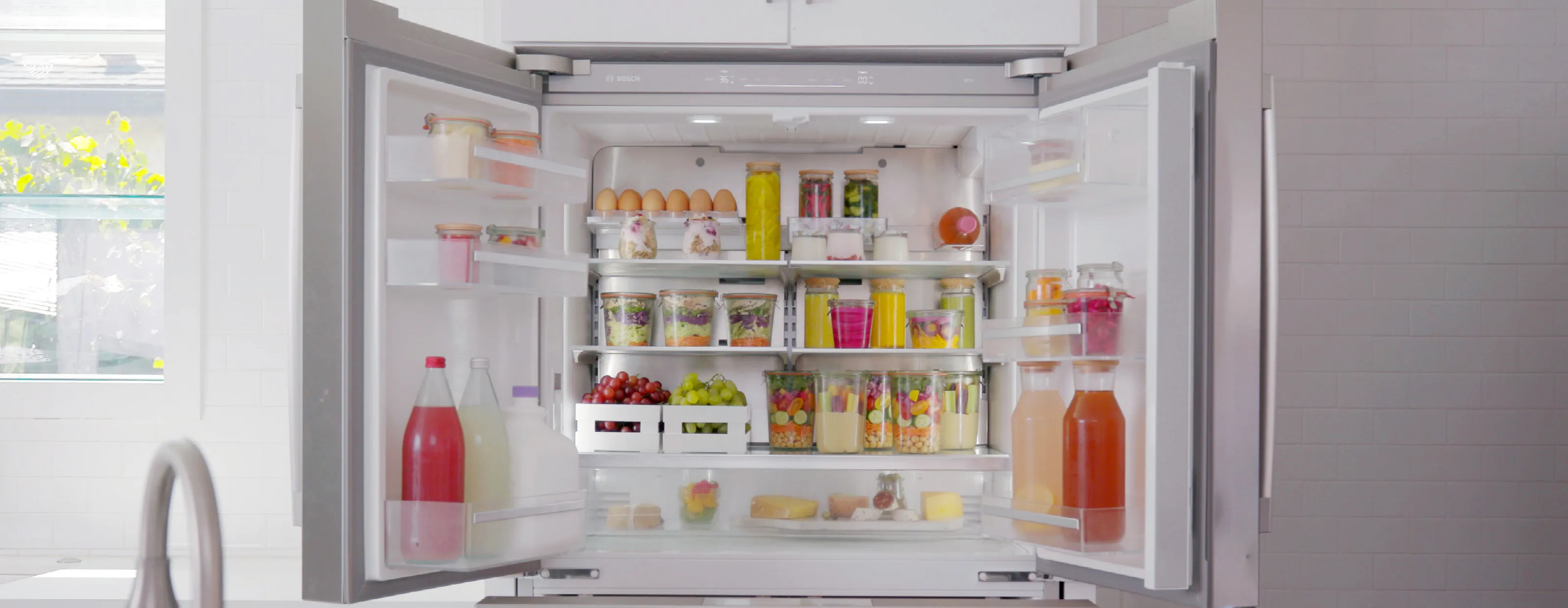 Open Bosch refrigerator with various food items, drinks, and storage containers neatly organized.