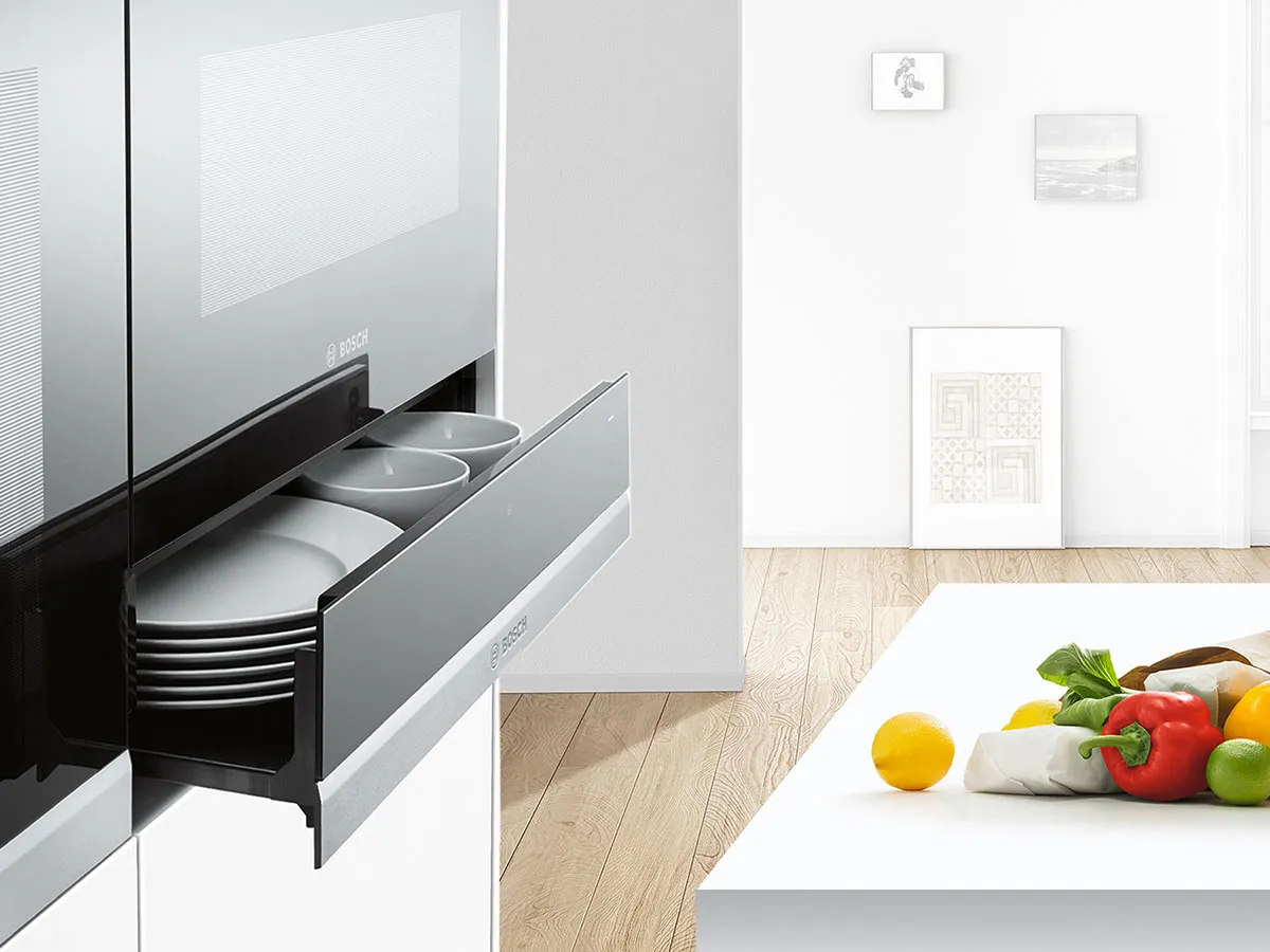 Modern kitchen featuring a sleek drawer with plates, alongside a bright table laden with fresh fruits and vegetables.