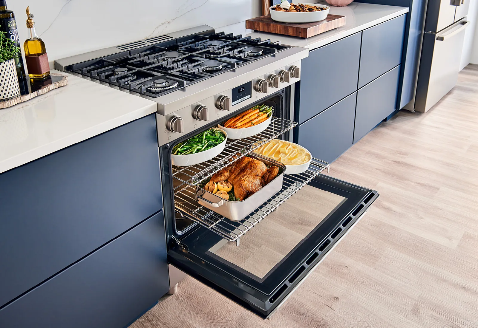 Open Bosch oven with roasted chicken, potatoes, carrots, and green beans on racks in a modern kitchen.