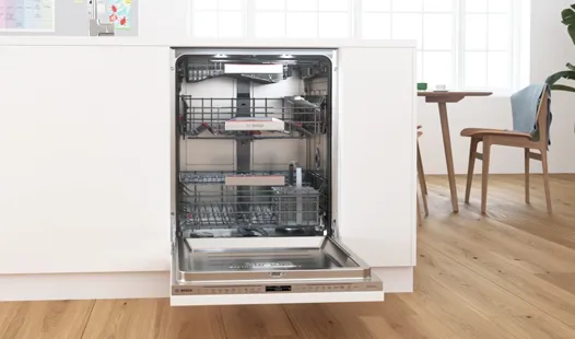 Open dishwasher with racks and shelves in a modern kitchen interior.
