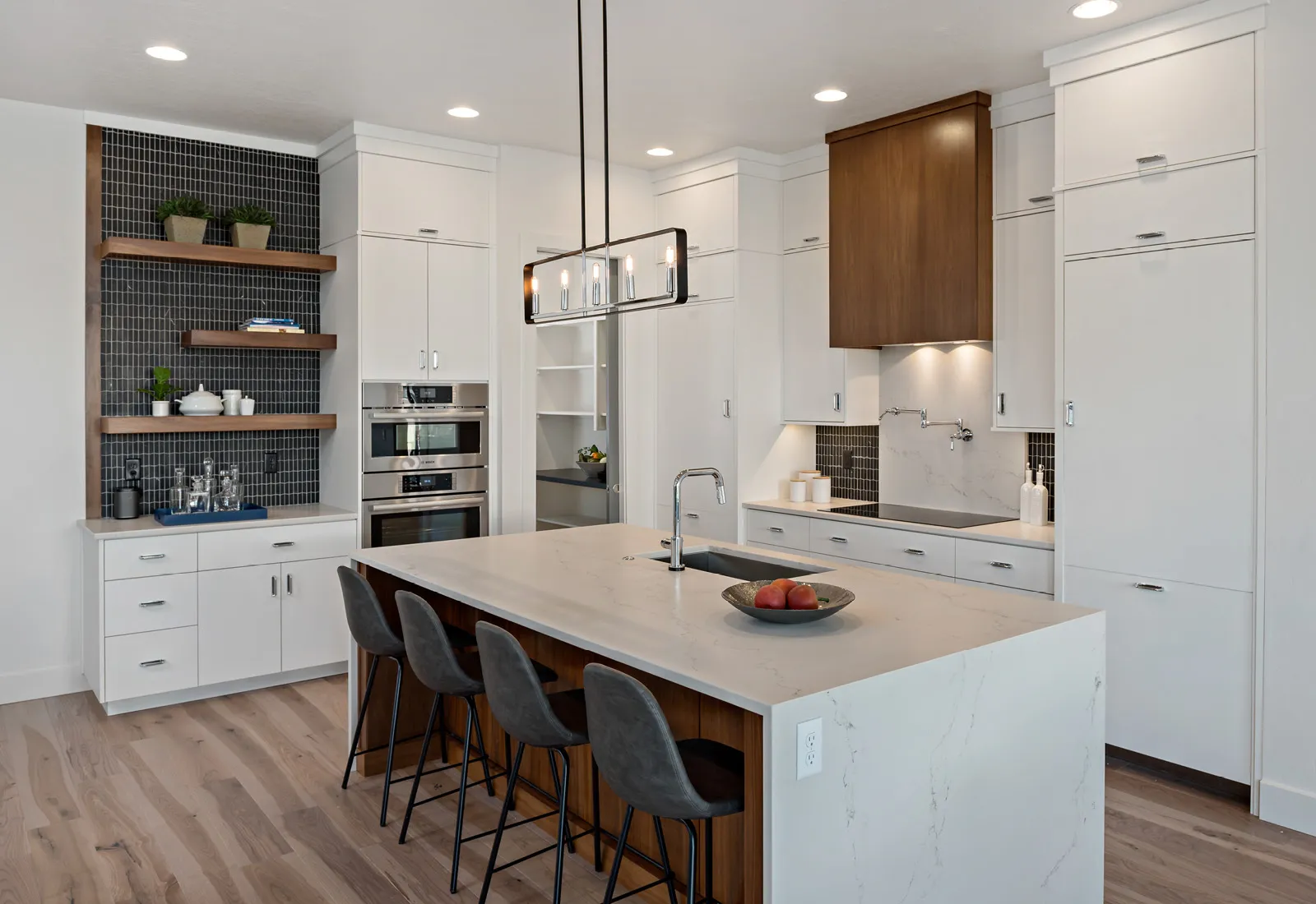 Modern kitchen with Bosch Custom Panel-Ready refrigerator blending in with white cabinets, white marble island, bar stools, and Bosch built-in appliances on wooden floor.