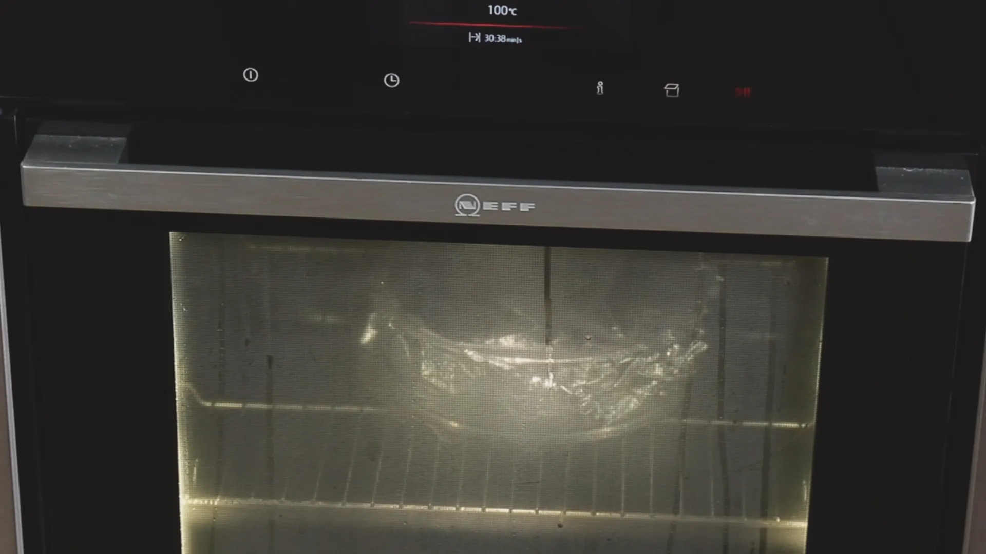 Inuti en ugn syns en glasform med lock, som står på en ugnsgaller, med temperaturen inställd på 100 grader Celsius.