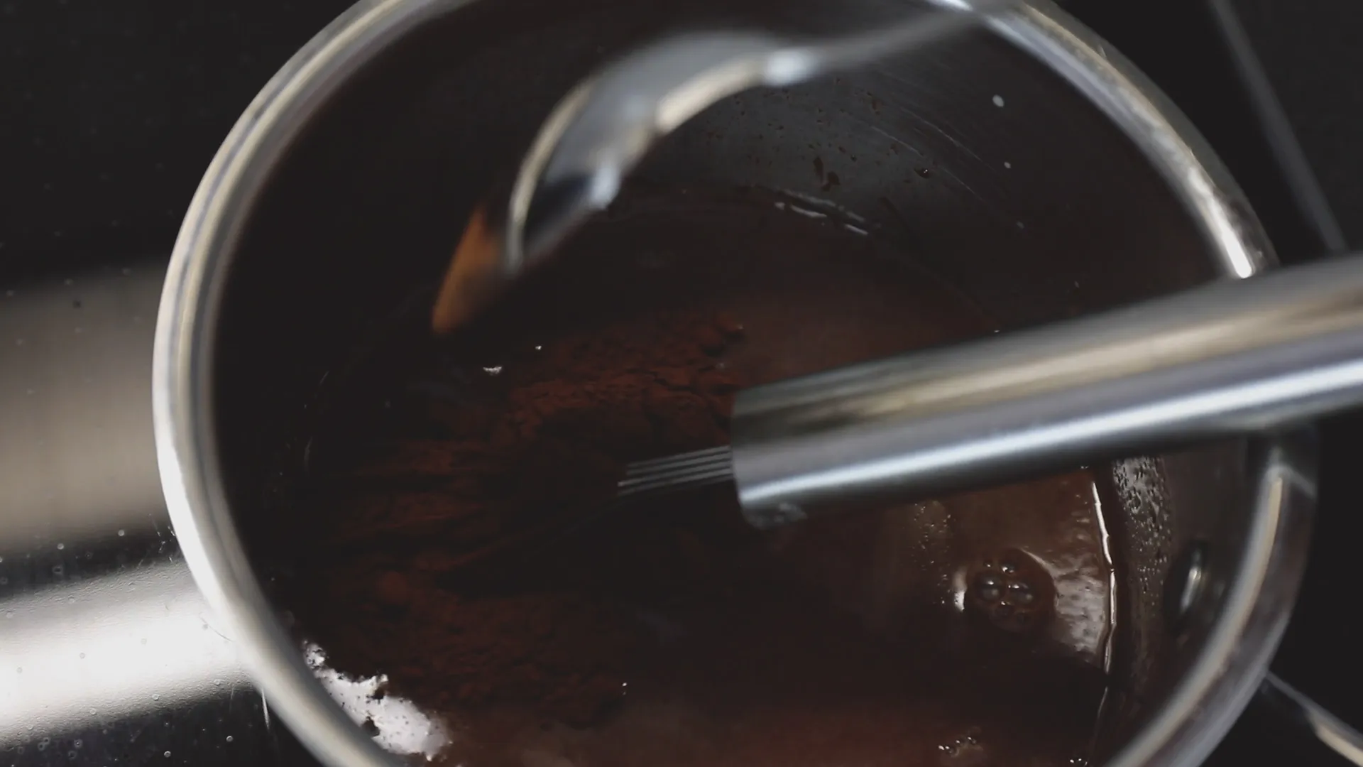 En kastrull med en glansig chokladsås, där en whisk vispar ner kakaopulver för att blanda ingredienserna.