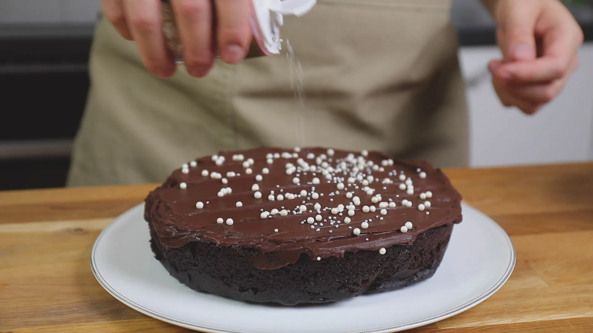 En kaka med chokladglasyr dekoreras med sockerpärlor medan en kock strör dem försiktigt på ytan för att ge en festlig touch.