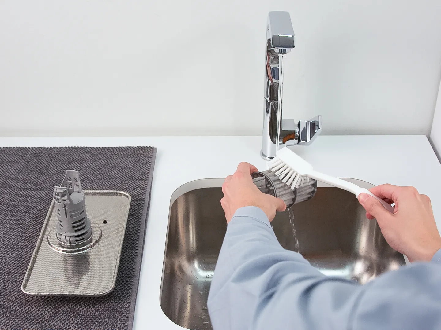 Person cleaning the inside of a Bosch dishwasher filter unit under running tap water.