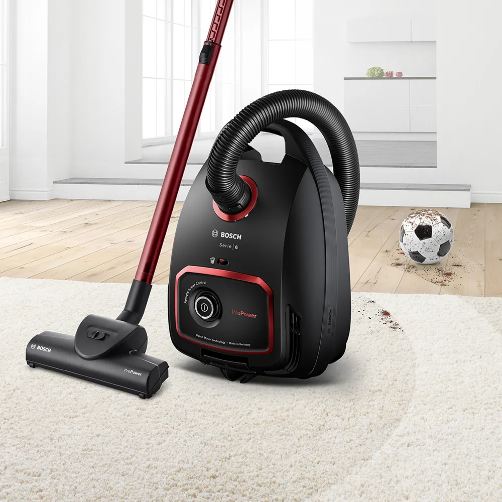 Прахосмукачка марка Bosch цвят черен и червен върху бял килим с футболна топка.