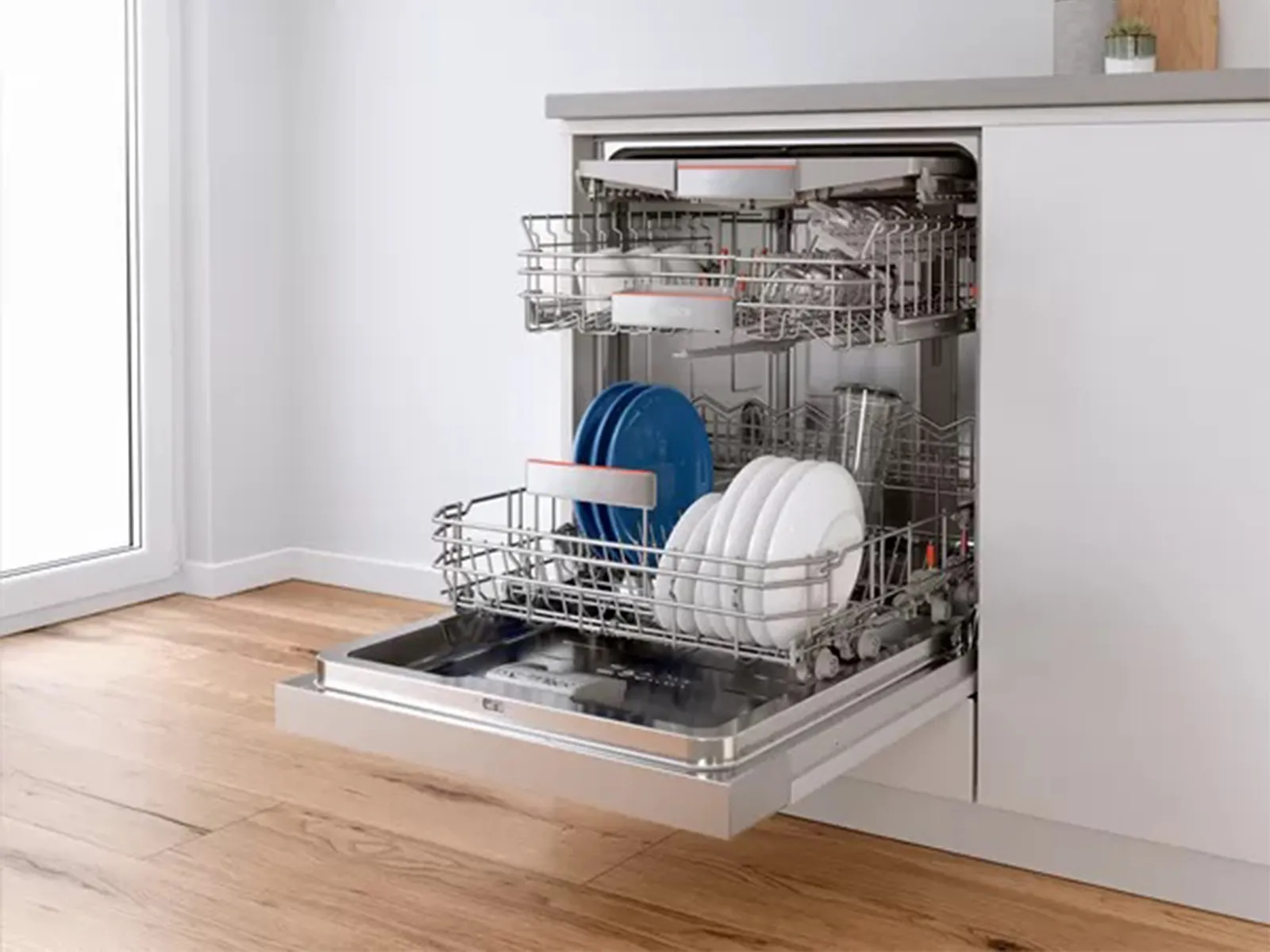 Open dishwasher with clean dishes and utensils inside on wooden floor.