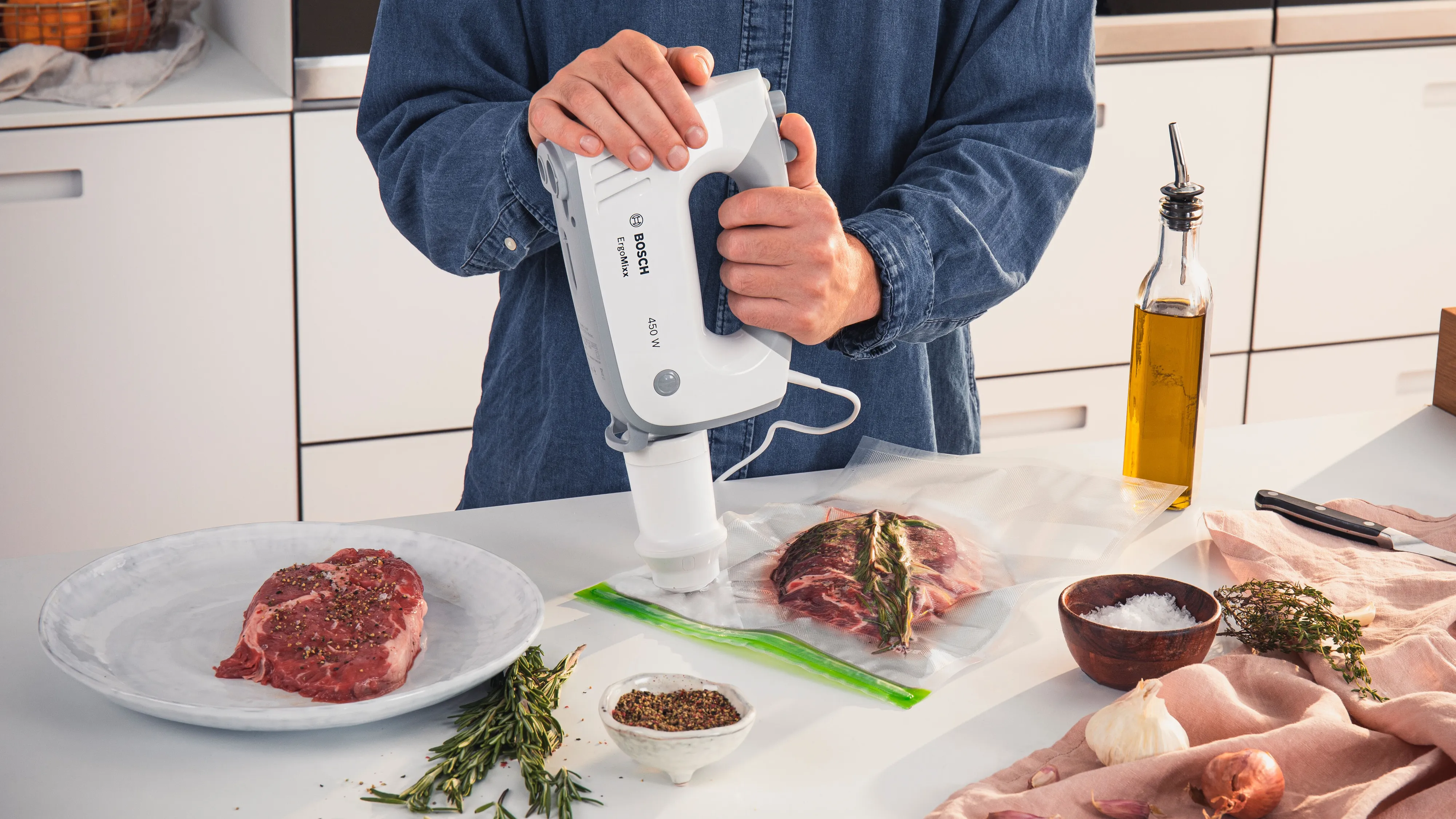O persoană care folosește un aparat de vidat alb pentru a vidă carne crudă aflată într-o pungă de plastic, așezată pe blatul din bucătărie, cu ierburi aromatice și condimente în apropiere