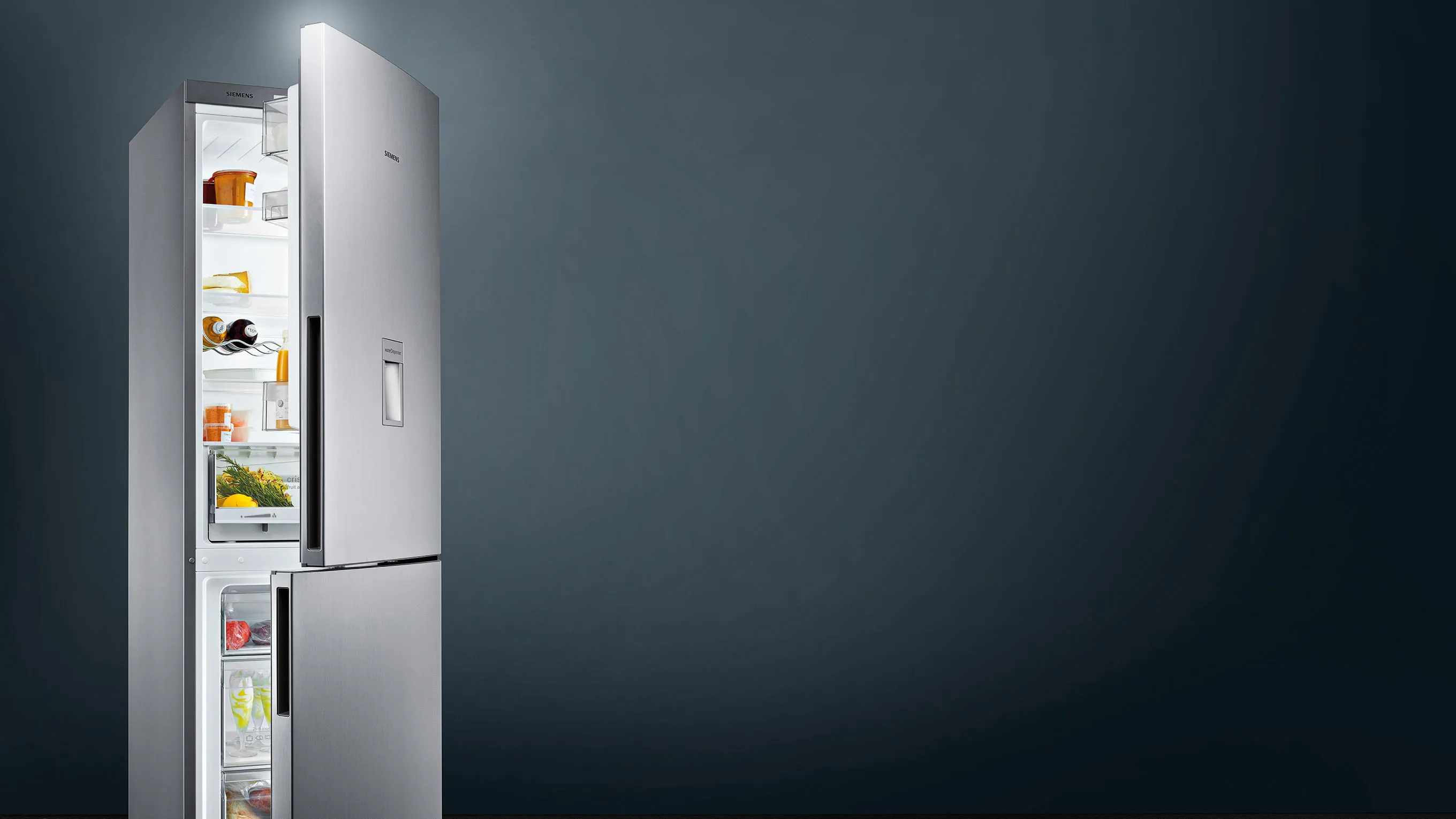 Stainless steel refrigerator with open door, revealing various food items inside, against a dark background.
