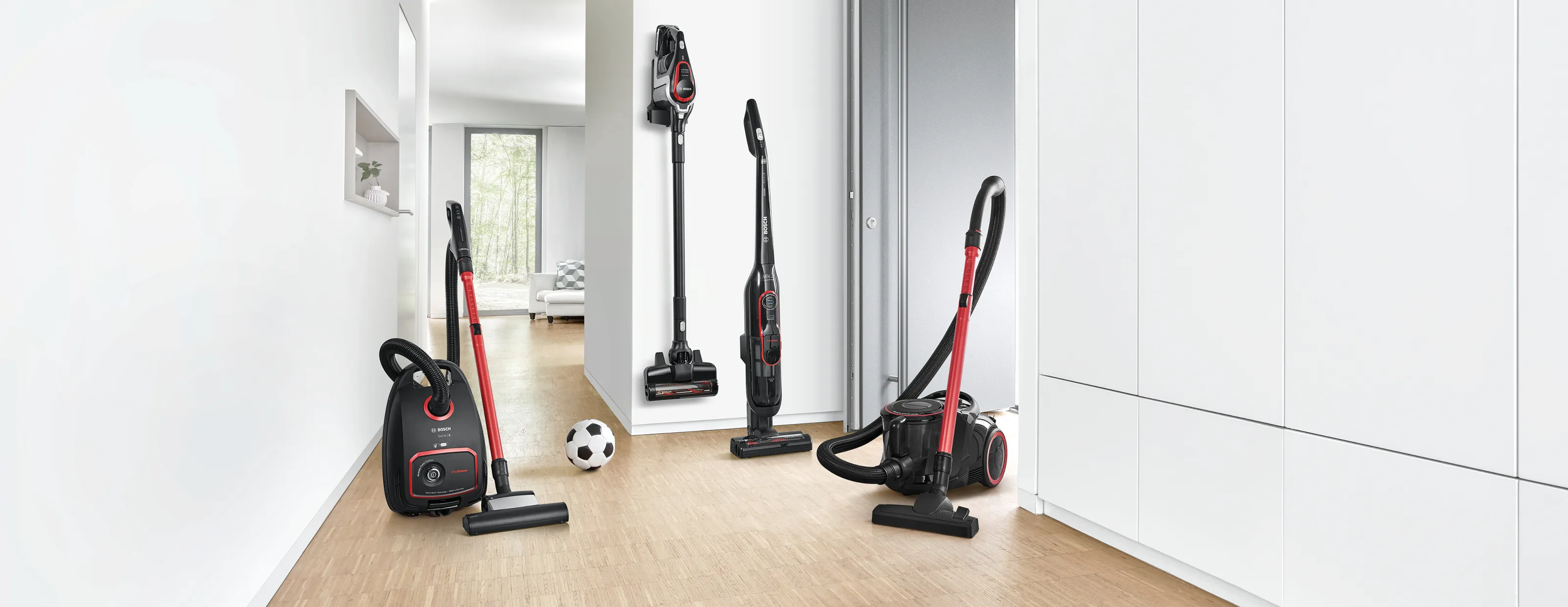 A lineup of four different vacuum cleaners in a bright hallway.
