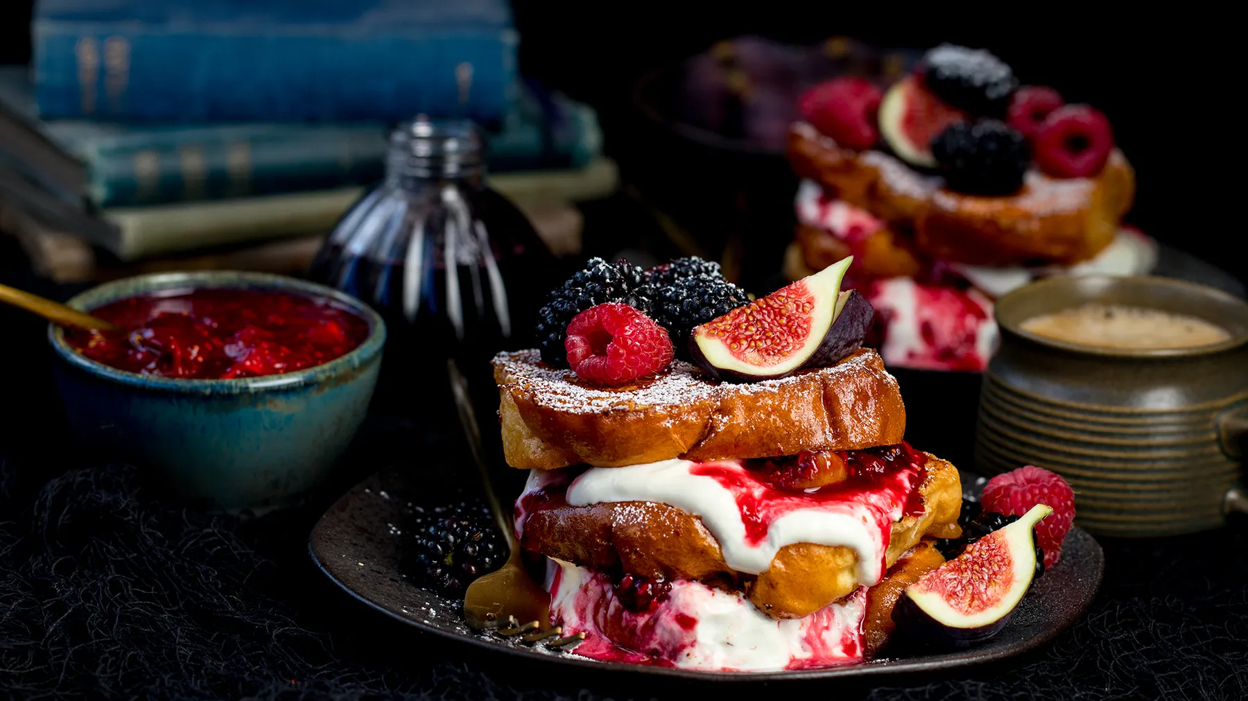 Decadent dessert plate with French toast, berries, figs, and creamy sauce on a dark background.