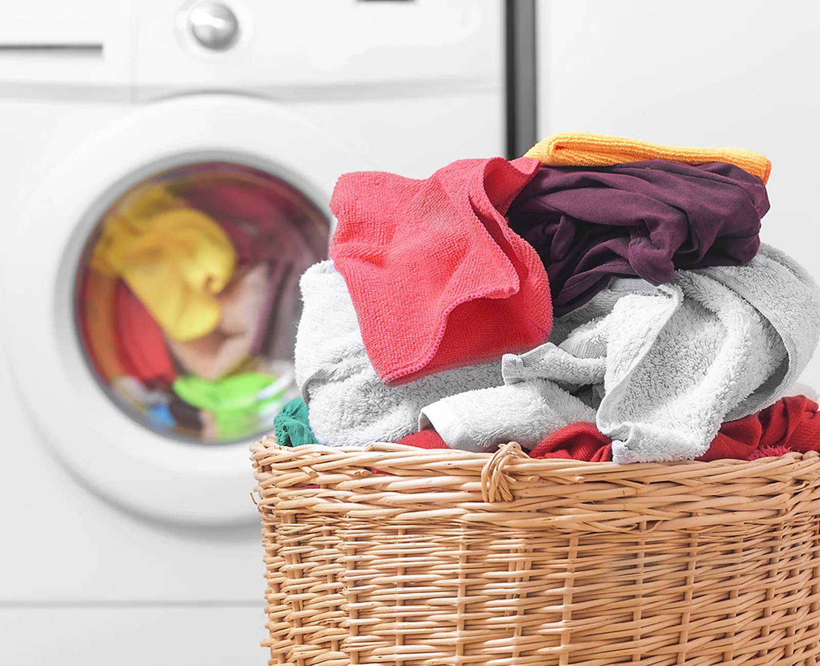 Laundry basket with colourful clothes in front of a washing machine.
