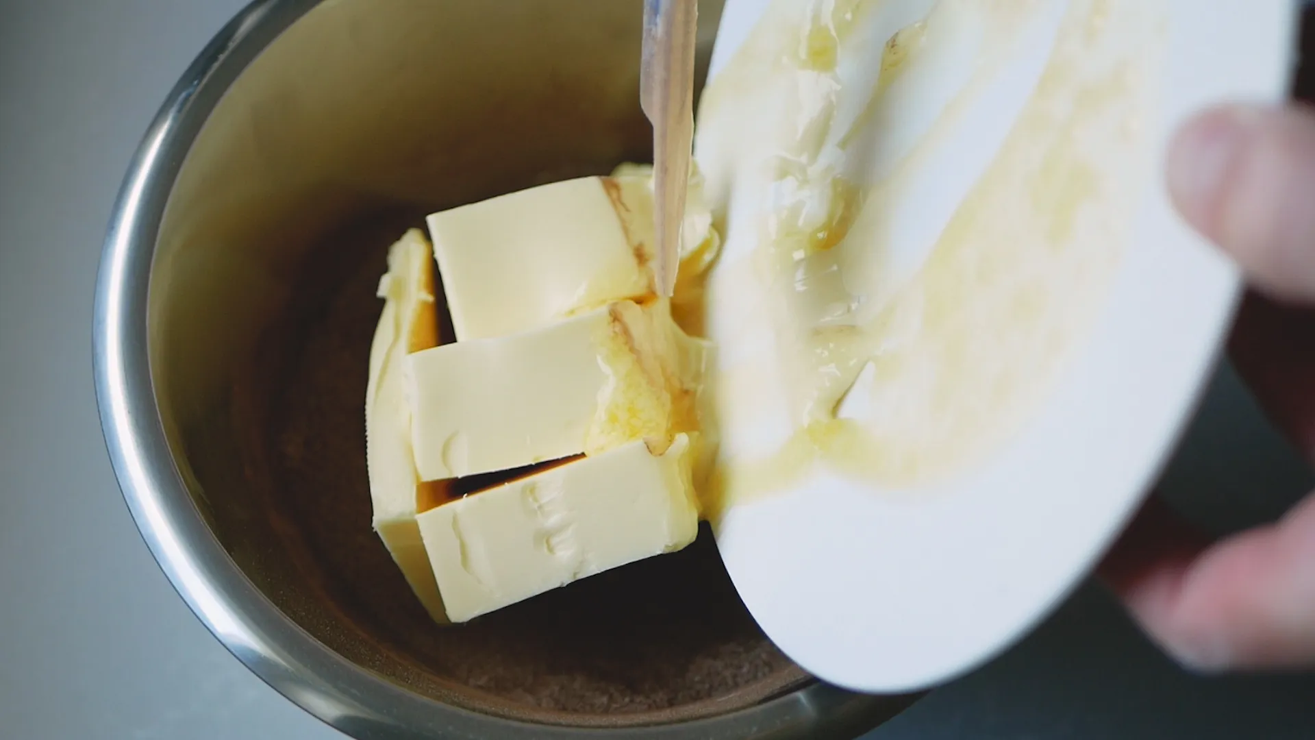 En skål med smör och socker som hällas samman, en vit tallrik hälls med smält smör över ingredienserna.
