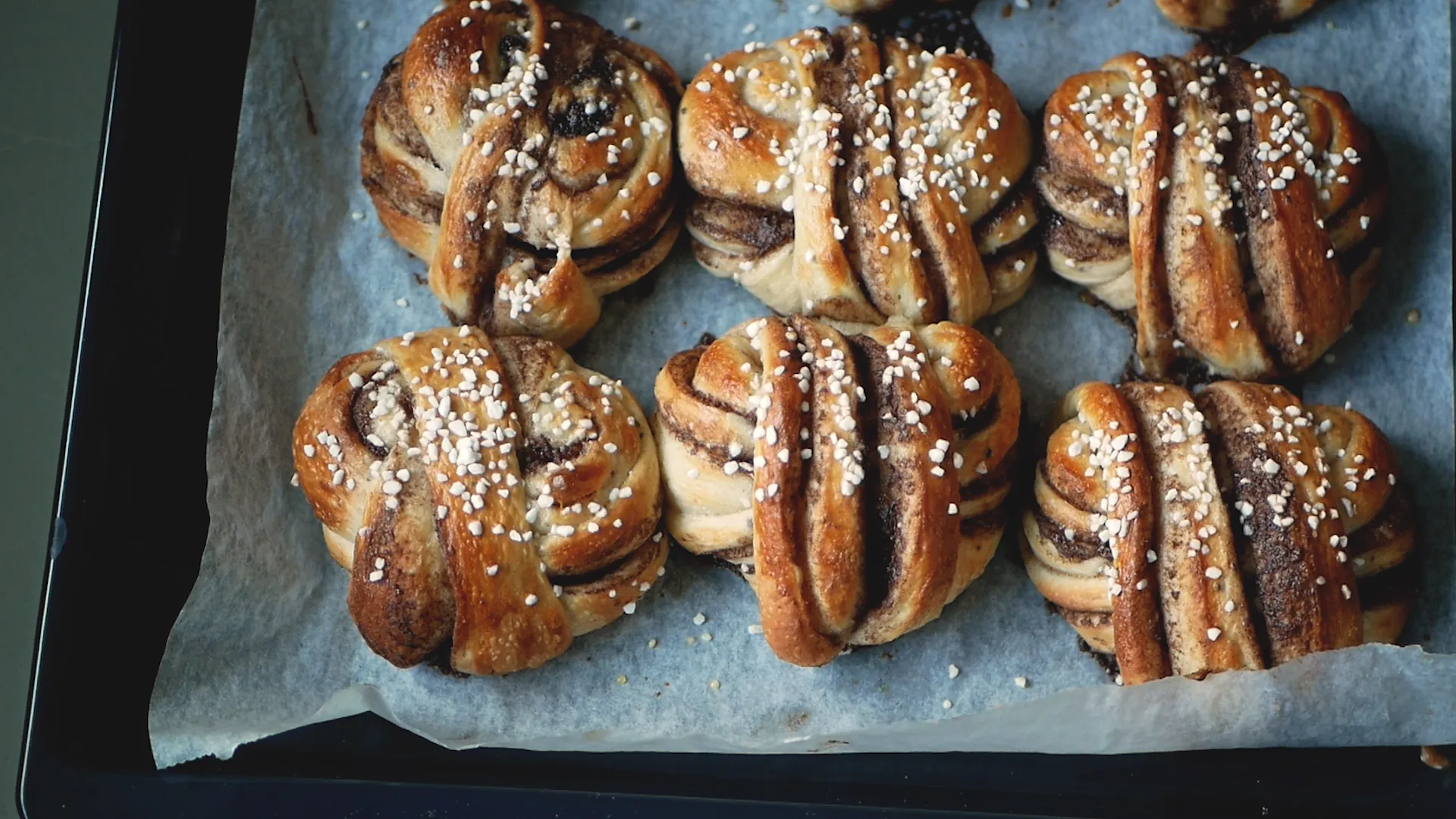 Grillade kanelbullar med glansig yta och mandelspån på en plåt, redo för att avnjutas.