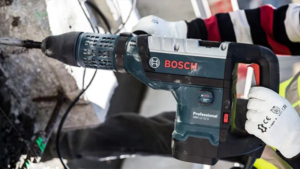 Taladro de potencia profesional Bosch, mano del trabajador de la construcción que sostiene la herramienta, fondo del sitio de la construcción.