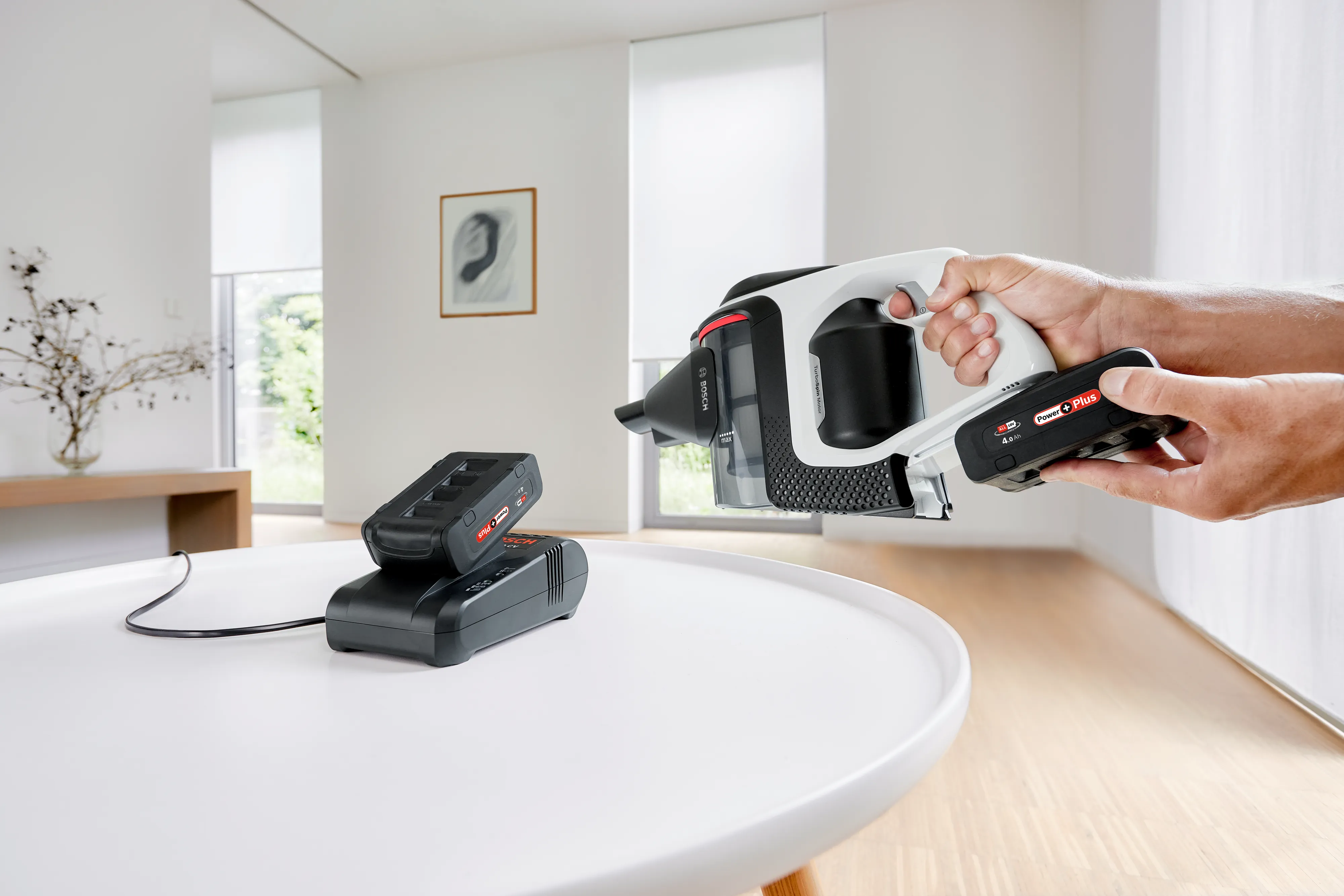 Încărcător rapid Bosch cu acumulator conectat și un aspirator Unlimited din care cineva se pregătește să scoată acumulatorul
