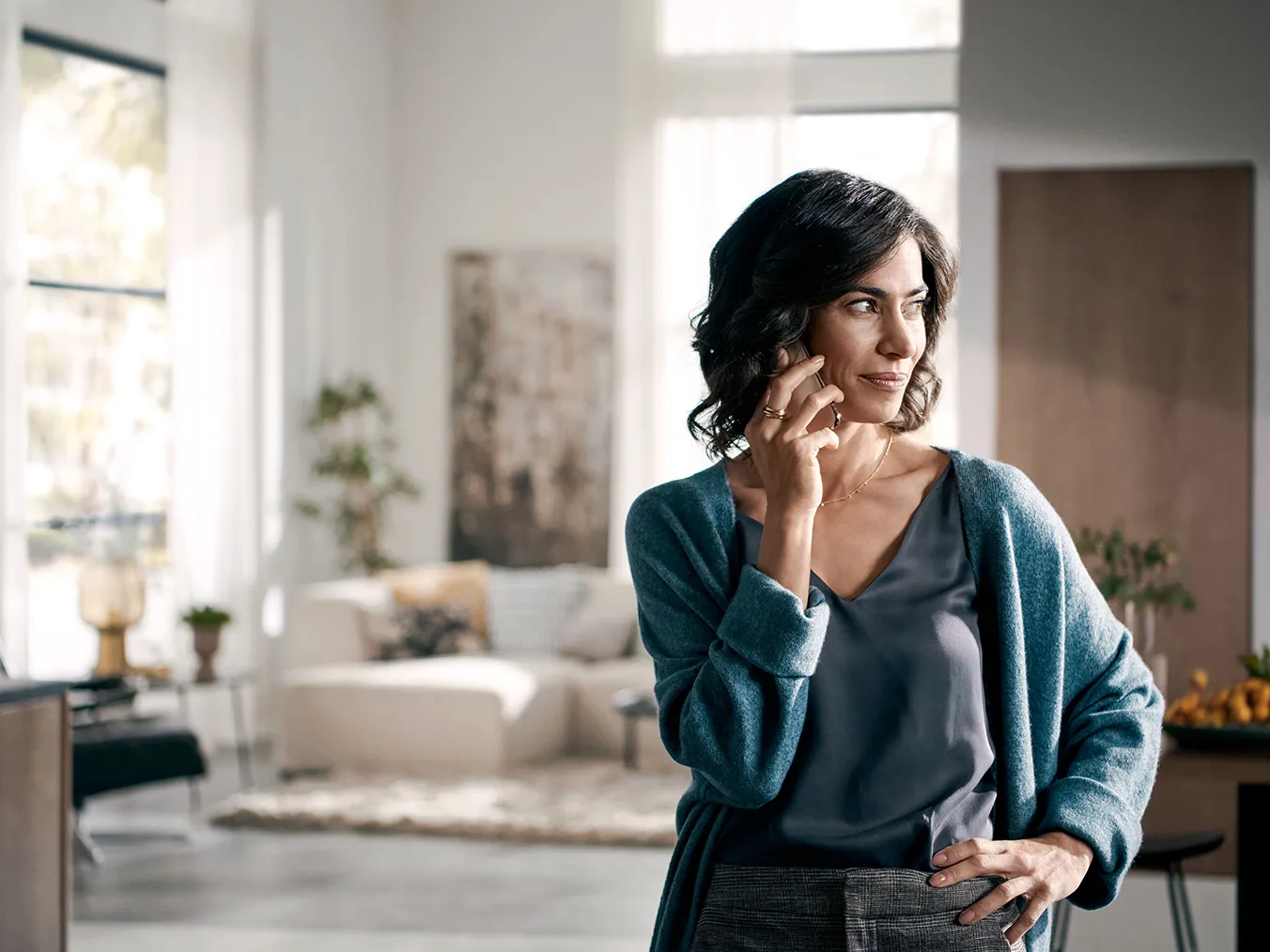 Woman in teal sweater standing in living room, thoughtful expression.