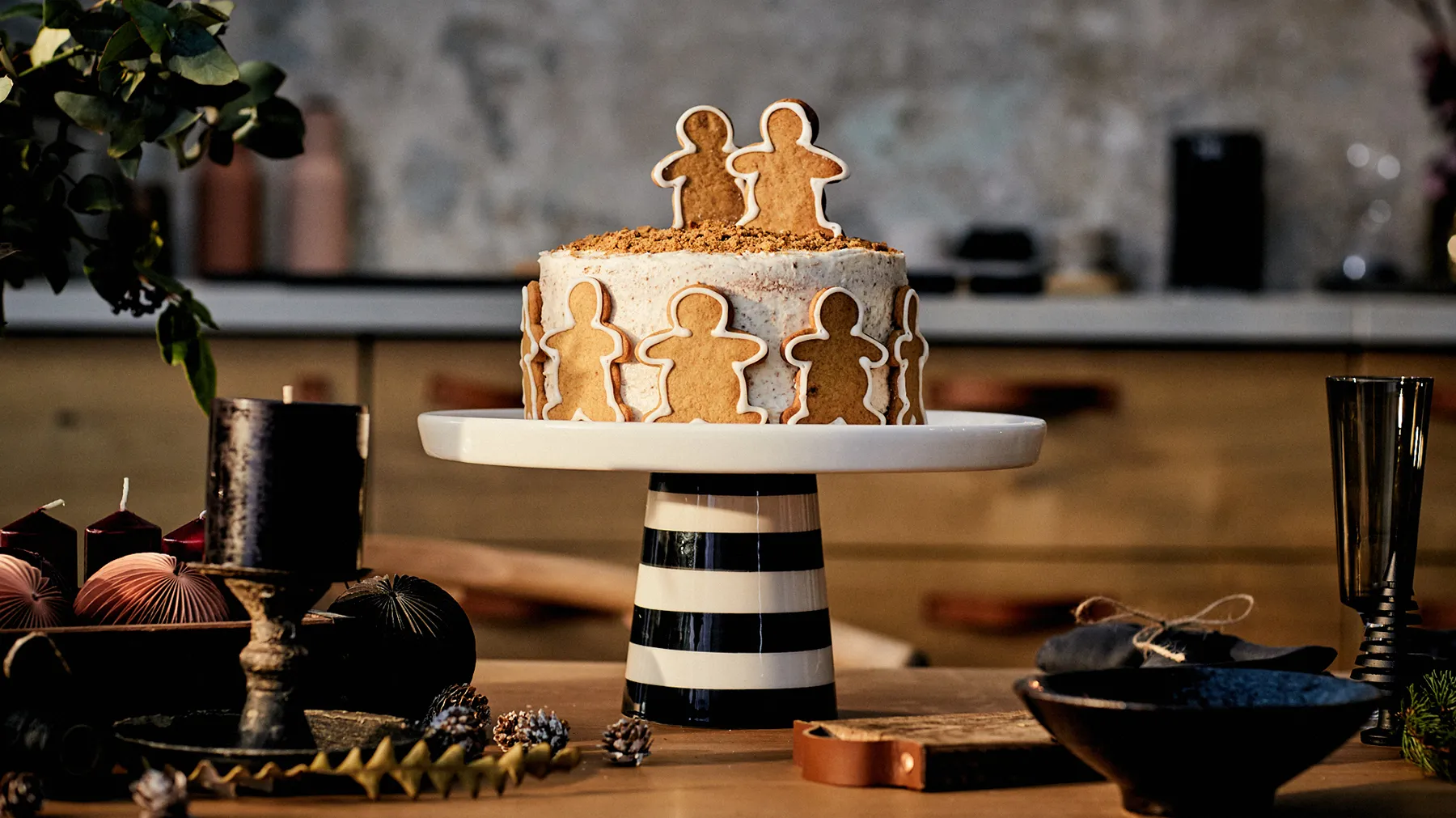 Gingerbread cake with gingerbread figures on a striped cake stand, surrounded by autumn decor.
