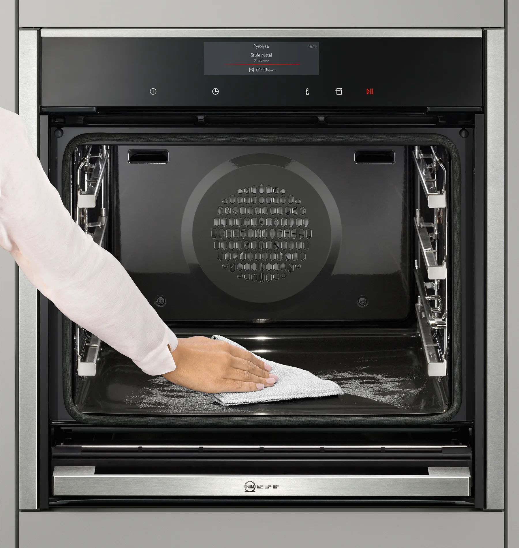 Close-up of a hand using a towel to wipe the inside of an open NEFF oven, cleaning the oven cavity and racks.