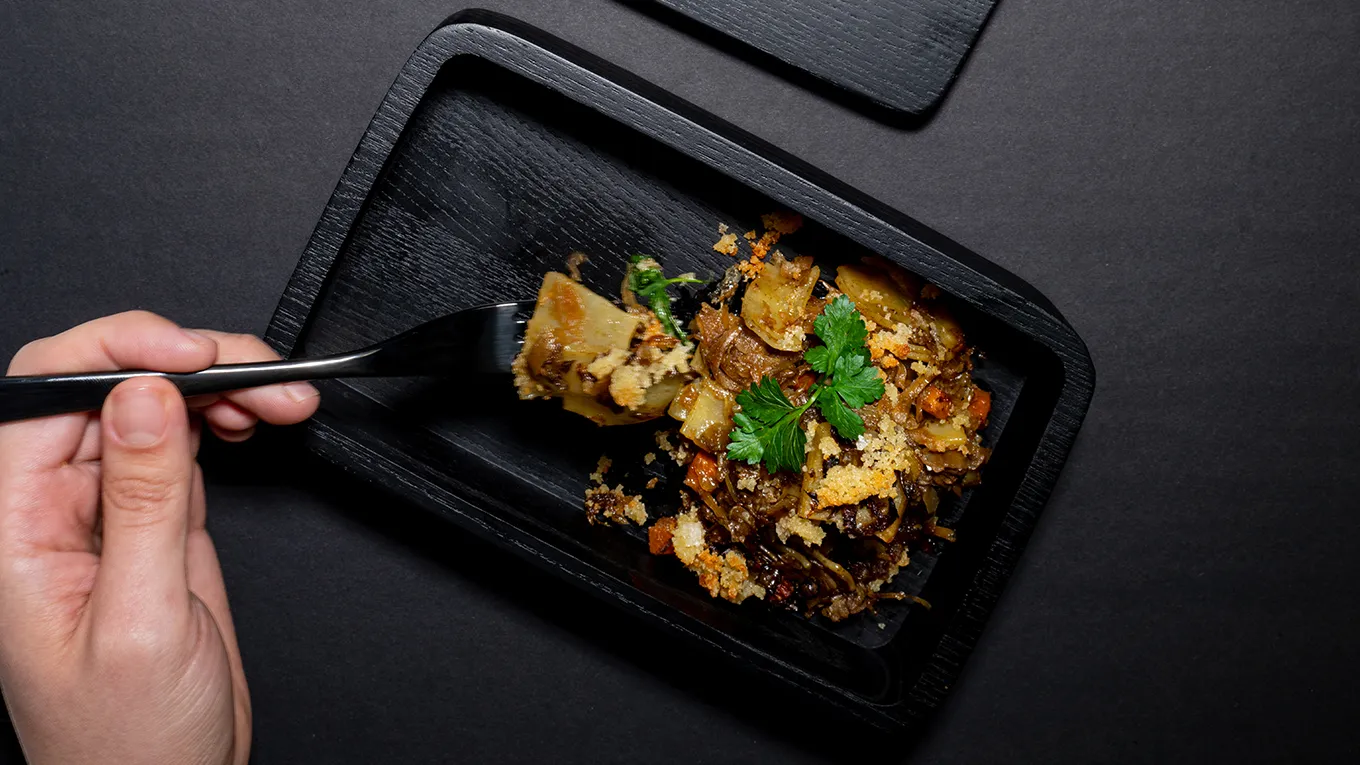 Savory dish with roasted vegetables, herbs, and chopsticks on a black plate.