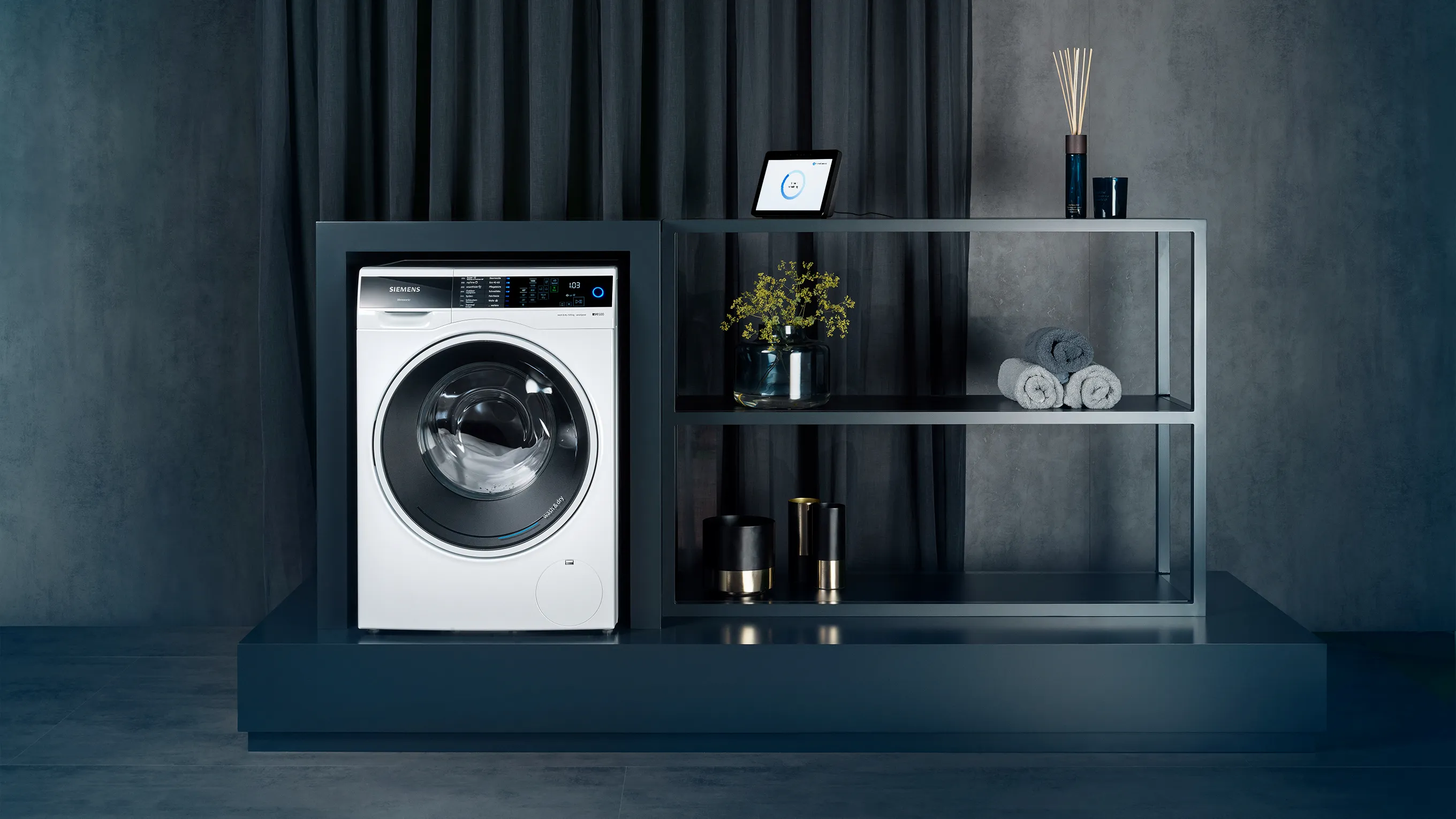 A Siemens washing machine next to a shelving unit with an amazon echo show