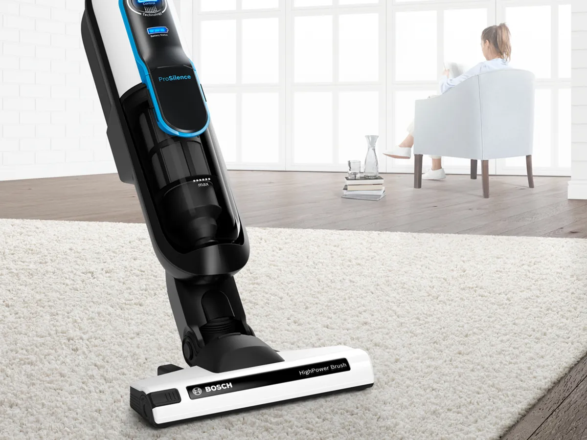 Vacuum cleaner in a living room with a person sitting in a chair.