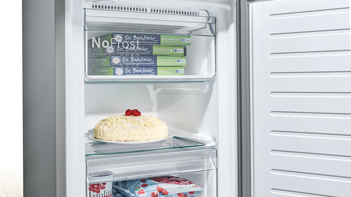Open refrigerator with cake, frozen food, and "No Frost" label on shelves.