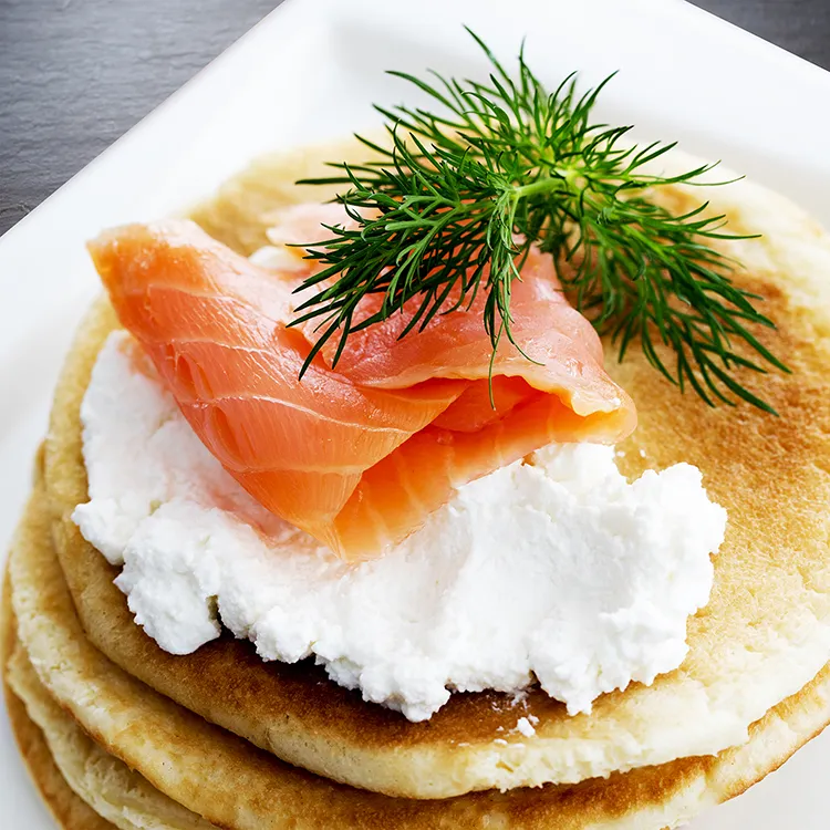 Pancakes topped with cream cheese, smoked salmon, and fresh dill garnish.