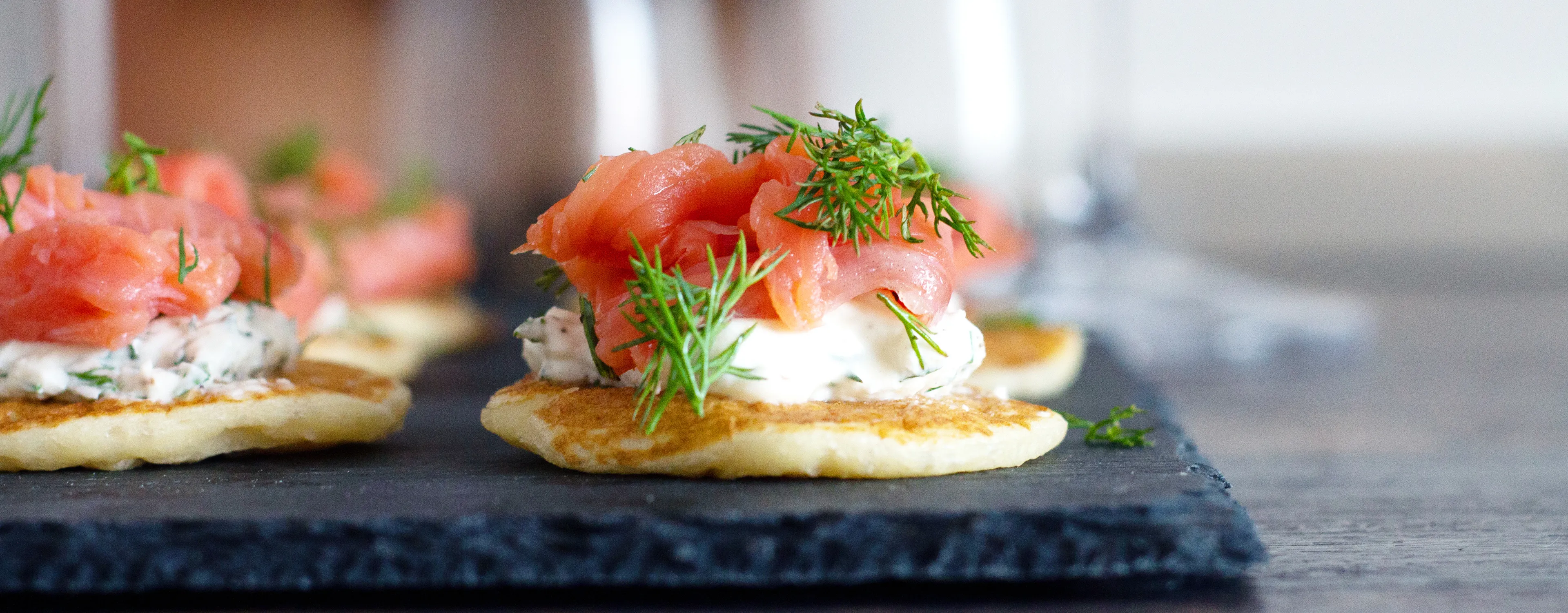 Smoked salmon, cream cheese, and dill on crackers, arranged on a slate board.