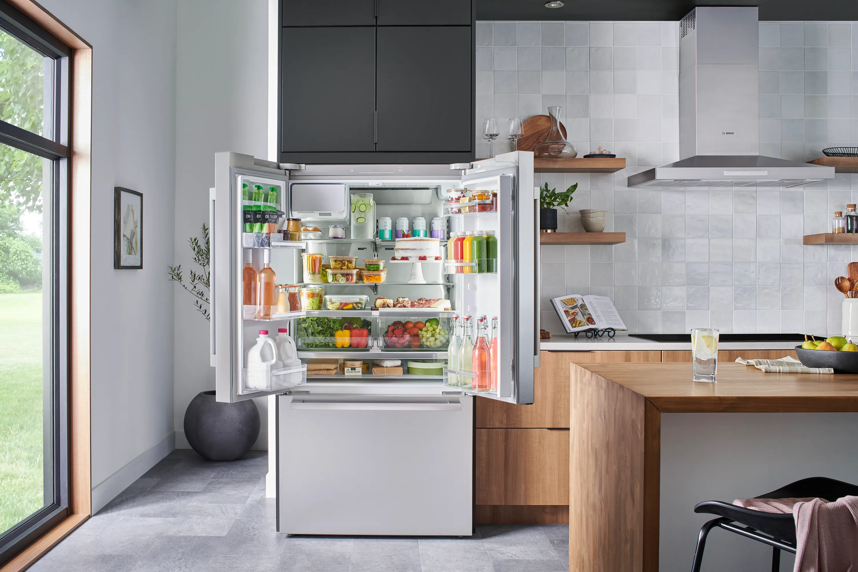 Modern kitchen with an open Bosch 36 inch stainless steel refrigerator filled with various food items and drinks.
