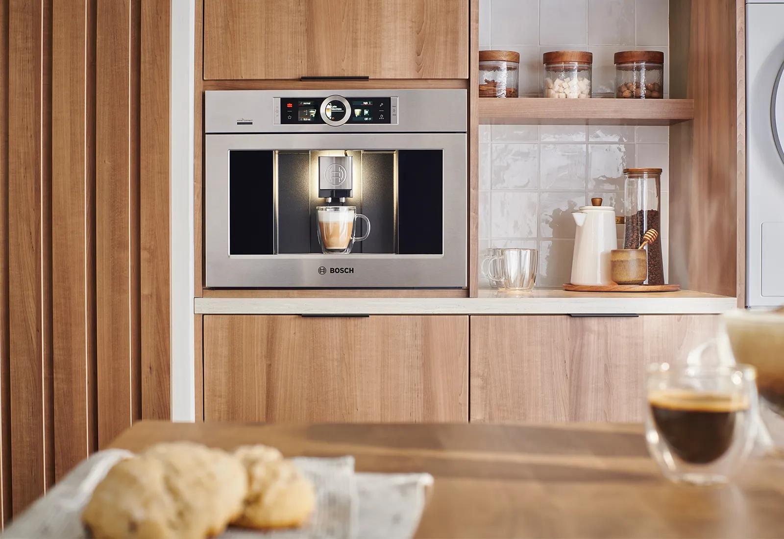 Bosch built-in coffee machine in a wooden kitchen, with a cup being filled under the dispenser.