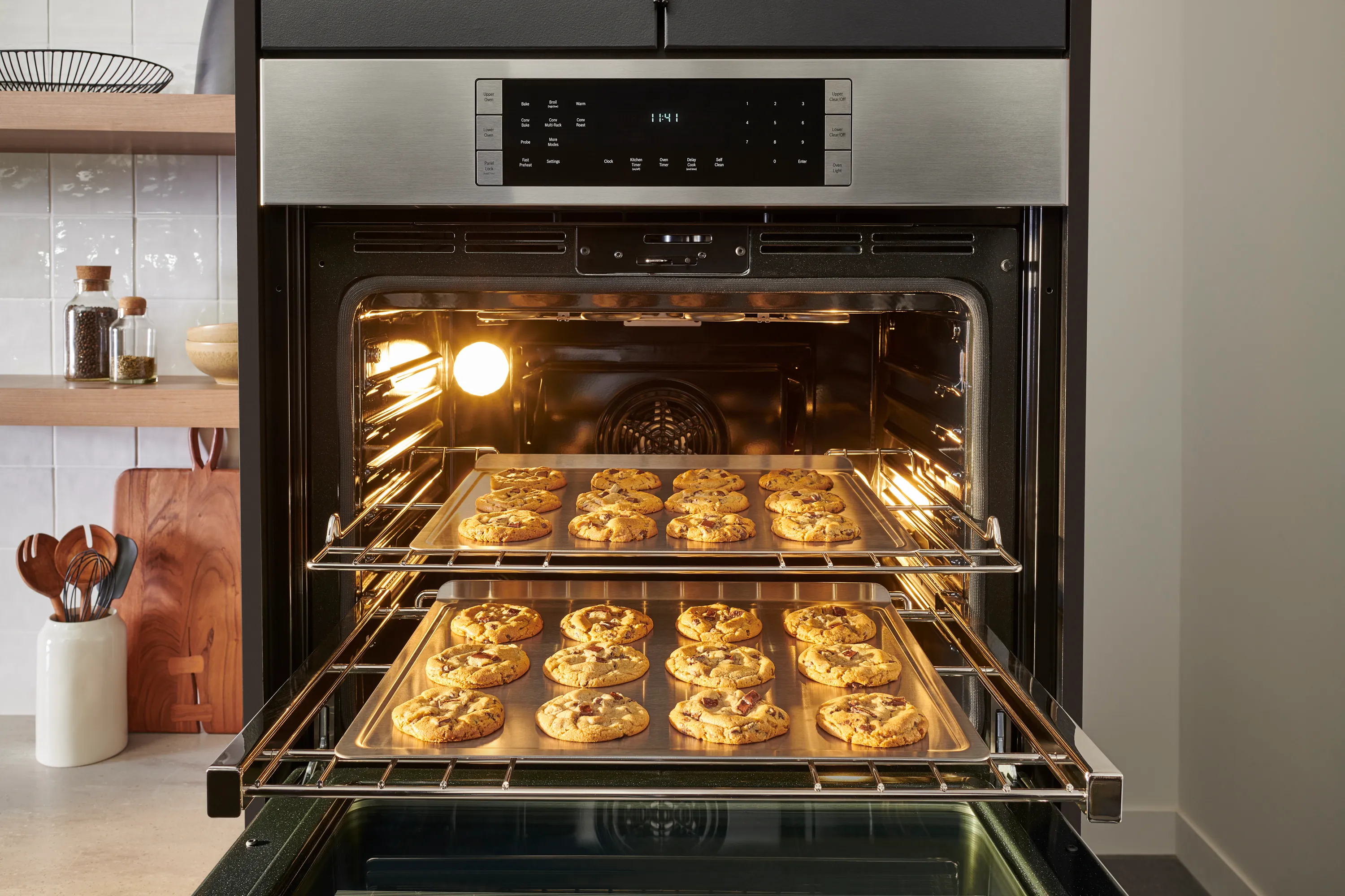 Open Bosch wall oven with two racks of freshly baked cookies, in a modern kitchen setting.